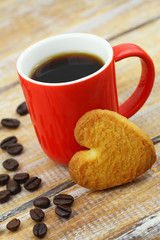 Heart shape cookie leaning against red much with black coffee
