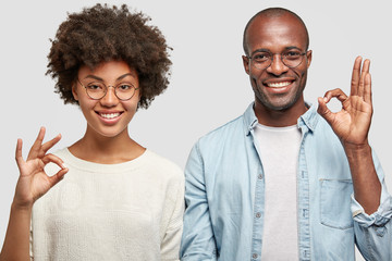 Cheerful African American couple make okay gesture, have positive expressions, show approval or...