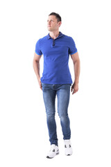 Serious young adult man in polo shirt walking forward towards camera and looking up. Full body isolated on white background. 