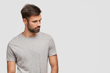 Indoor shot of concentrated handsome unshaven young male foused aside, has muscular body, dressed...