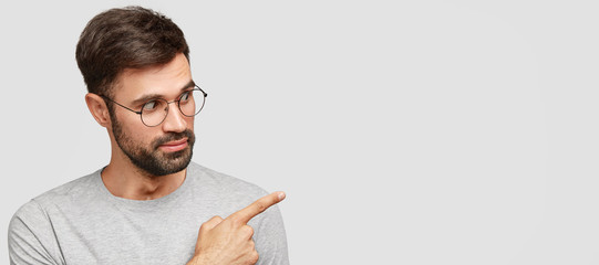 Horizontal portrait of surprised male professor with thick beard, points at upper right corner with...