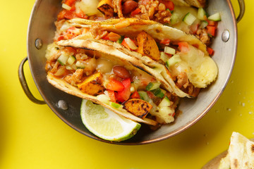 Close up of mexican tacos with chili con carnes and grated cheese served over a yellow background