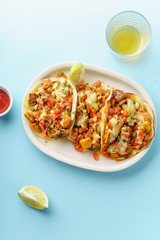 Overhead image of mexican tacos with chili con carne, sweet potatoes and grated cheese served over a blue background