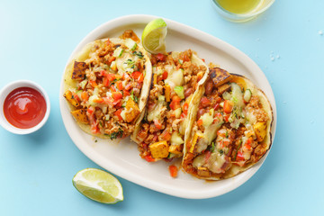 Overhead image of mexican tacos with chili con carne, sweet potatoes and grated cheese served over a blue background