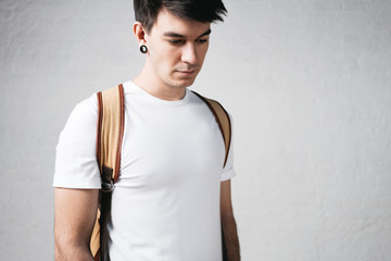 Close-up view of pensive man wearing white t-shirt and backpack. Studio portrait