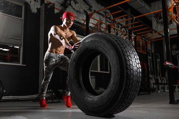 Shirtless man flipping heavy tire at gym