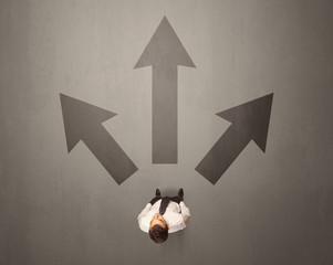 Young contemplating businessman stands in front of brown arrows © ra2 studio