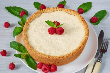 Homemade cheesecake with fresh berries on the white plate decorated with raspberries, mint leaves, knife and fork on the gray background. Healthy summer dessert. Close up view