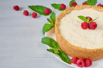 Homemade cheesecake with fresh berries on the white plate decorated with raspberries, mint leaves, knife and fork on the gray background. Healthy summer dessert. Side view with copy space for text