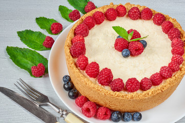 Homemade cheesecake with fresh berries on the white plate decorated with raspberries and blueberries, mint leaves on the gray background. Healthy summer dessert. Close up view 