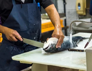 Fotobehang man fileert zalm op witte snijplank, de chef-kok die vis aan tafel snijdt © Voy_ager