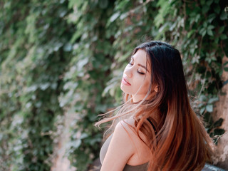 Naklejka premium Portrait of young attractive girl with smile. Woman with oriental face, brown eyes and stylish ombre dyed long haistyle on foliage background. Street style.