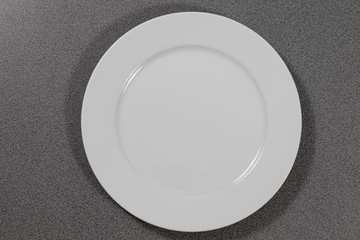 Weißer flacher Porzellanteller auf einem grauen Tisch 