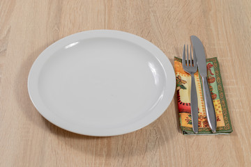 Messer und Gabel auf einer Serviette neben einem weißen Porzellanteller 