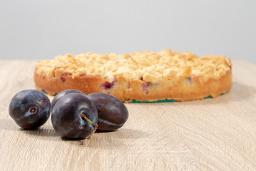 Frische reife Pflaumen vor einem fertigen Pflaumenkuchen auf einem Holztisch