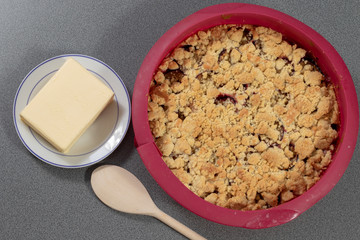 Frischer Pflaumenkuchen in Silikonbackform neben einem Stück Butter und einem Kochlöffel aus Holz