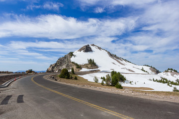 A scenic highway (Rim Drive) with the rocky mountain (Watchman Peak) background in Crater Lake National Park, Oregon, USA