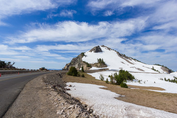 A scenic highway (Rim Drive) with the rocky mountain (Watchman Peak) background in Crater Lake National Park, Oregon, USA