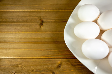 Eggs on a while plate sitting on the kitchen table waiting to be cracked