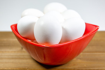 A group of eggs inside a deep red bowl waiting for the chef to use them in a meal