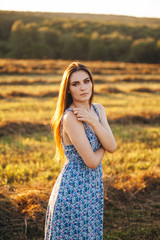 Fototapeta na wymiar Beautiful young girl in a long sundress at sunset in the fields posing.