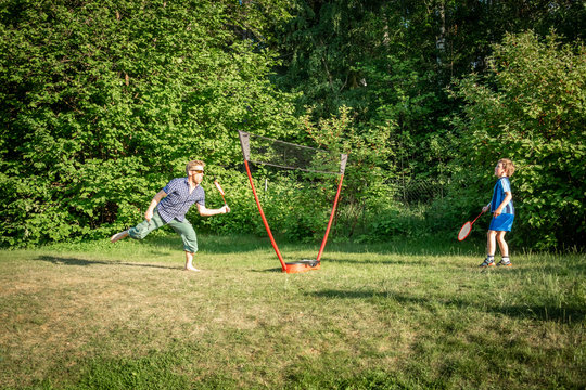 Motion of one adult male and a young boy playing badminton otudoors on a lawn with trees in the background.