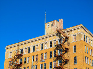 Obraz premium Old building facade and a emergency staircase in Greenville, TX, USA. Color view of a red brick wall with metal fire escape against clear blue sky on bright sunny day.