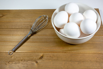 Fototapeta na wymiar A group of eggs inside a deep white bowl next to a whisk waiting for the chef to use them in a meal