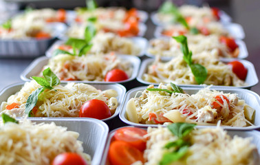 preparation of dietary dishes in the kitchen for the delivery of dietary lunch, basil, tomato cherry,  cheese, pasta and chicken fillet. concept of takeaway food. selective focus