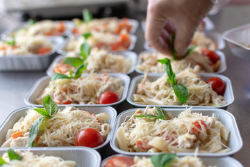 preparation of dietary dishes in the kitchen for the delivery of dietary lunch, basil, tomato cherry,  cheese, pasta and chicken fillet. concept of takeaway food. selective focus