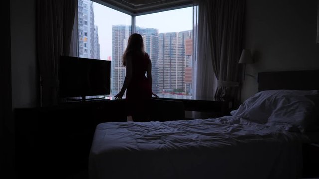 Woman get up from bed and look aut on window on Hong Kong skyscrapers