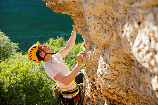 Image of tourist man in helmet climbing up mountain