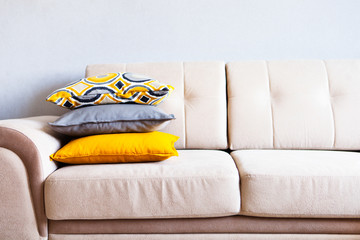 Multi-colored pillows on a beige fabric sofa, the concept of home comfort and cozy, copy space, close up