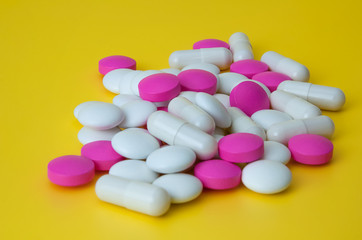 Obraz na płótnie Canvas A pile of pills of white and pink on a yellow background.