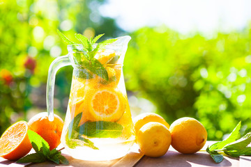 Summer fresh cold drink beverages. Ice Lemonade in the jug and lemons and orange with mint on table
