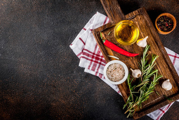 Cooking background, herbs, salt, spices, olive oil on cutting board, dark rusty background copy space top view