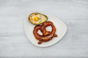 Eggs baked in avocado on plate with pretzel