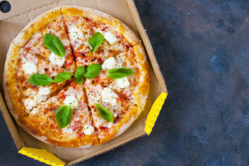 Homemade pizza with tomatoes, mozzarella and basil. Top view with copy space on dark stone table.