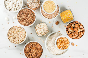 Selection various types cereal grains groats  in different bowl on white marble background, copy space