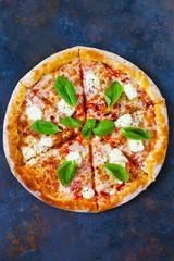 Homemade pizza with tomatoes, mozzarella and basil. Top view with copy space on dark stone table.