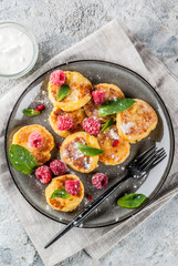 Healthy summer breakfast, cheese pancakes with raspberry, powdered sugar and mint, grey concrete background copy space
