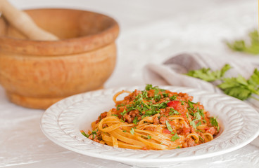 A plate of Tagliatelle with ragu sauce. Background: a wooden pestle.