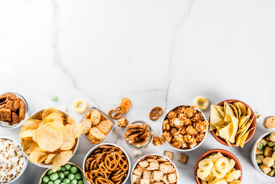 Variation different unhealthy snacks crackers, sweet salted popcorn, tortillas, nuts, straws, bretsels, white marble background copy spaceealthy snacks
