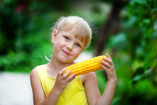 The lovely girl in a yellow dress holds corn in hand