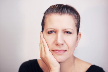 A good middle-aged woman on a gray background holds her cheek and suffers from toothache and headache