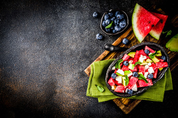 Obraz na płótnie Canvas Summer food concept, fresh cold watermelon salad with feta cheese, blueberry, avocado and mint, dark rusty background copy space