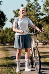 Obraz premium Having break. Positive delighted blonde keeping smile on her face and wearing uniform while going to ride the bicycle