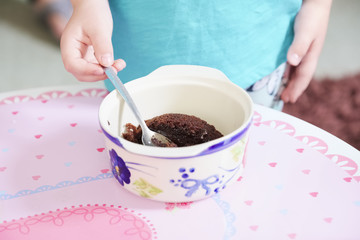 Fototapeta na wymiar Child eating sweets pudding desert chocolate cake young kid girl with spoon and dish unhealthy