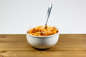 Spaghetti Bolognese in a deep white bowl on the wooden kitchen table waiting to be eaten