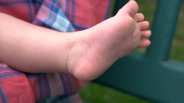 Bare feet of infant baby in park. Mother holding her newborn baby. Tiny leg of newborn.